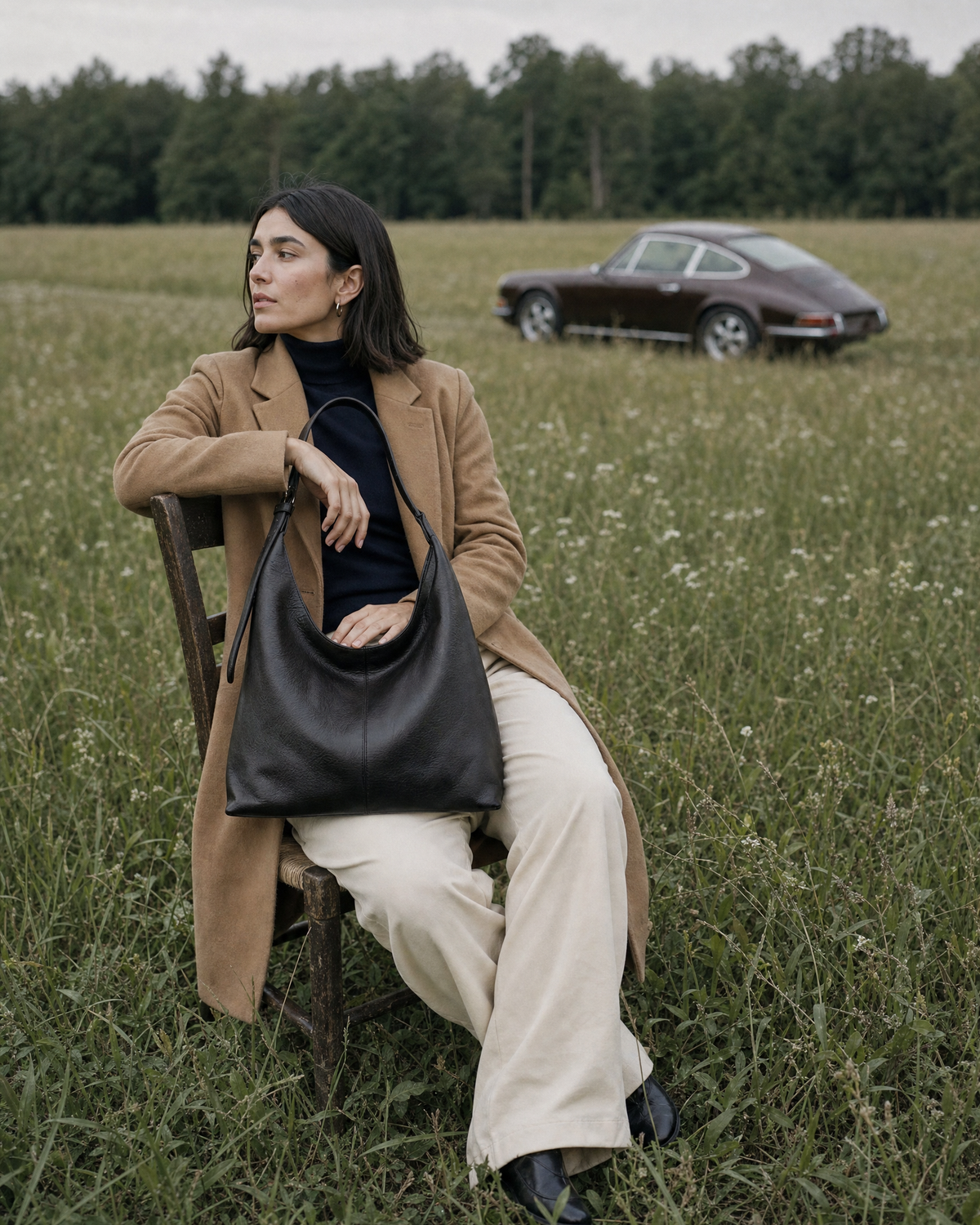 Woman sitting sideways on a wooden chair in a meadow with The Houle in Noir on her lap