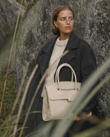 Woman leaning against a mossy boulder with The Aurore Briefcase in Écru