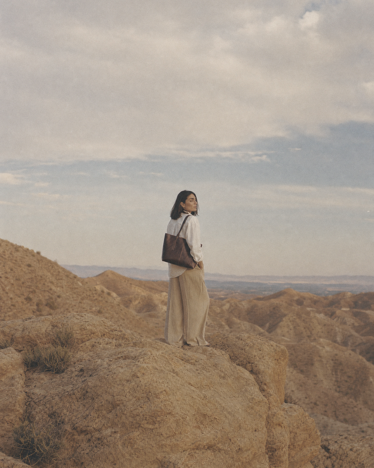 Woman standing on a rock in a wide dry landscape with The Marée A4 tote