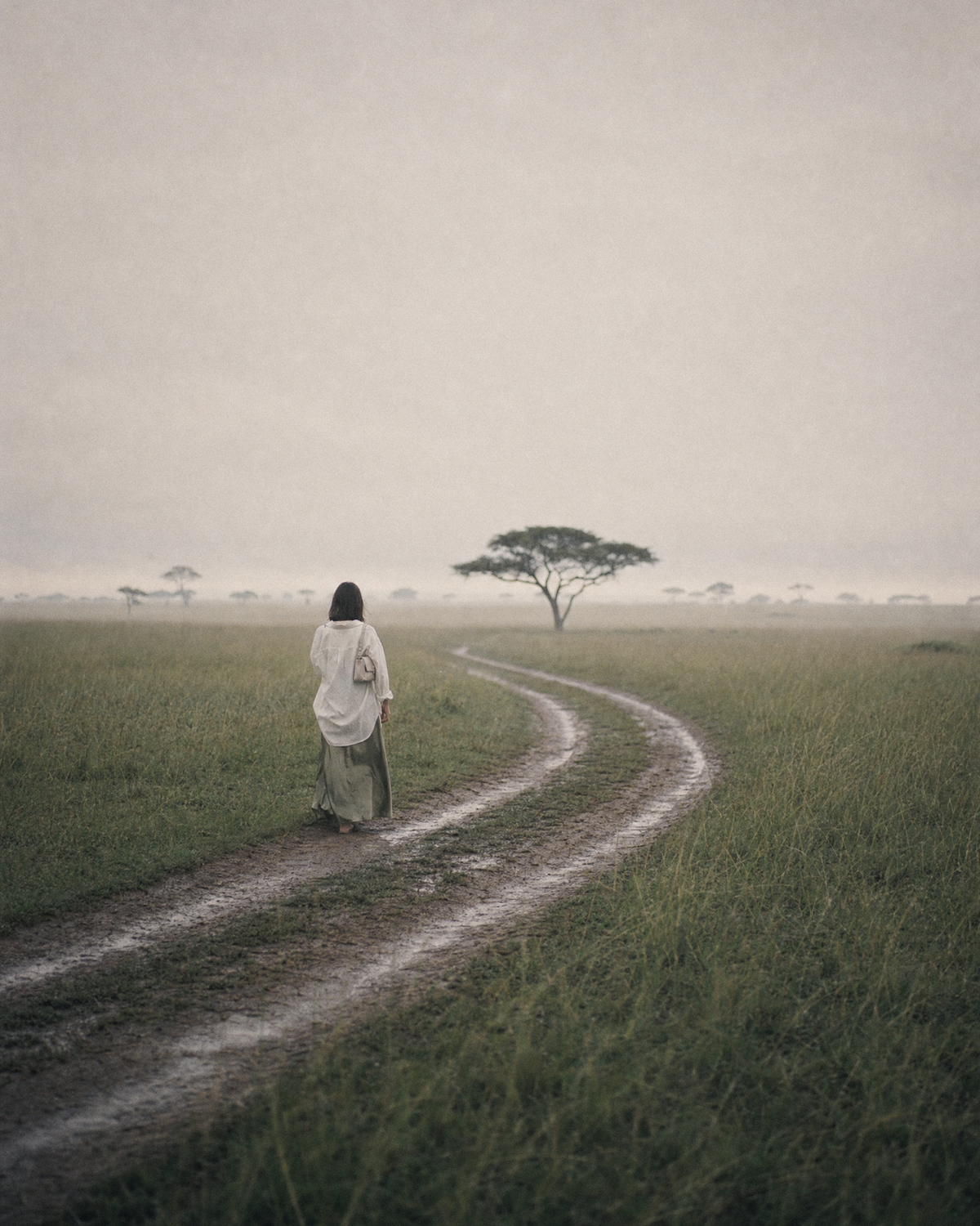 Woman walking along a dirt track through the savanna with The Brise in Écru