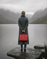 Woman by a misty loch holding The Aurore Briefcase in Rouge behind her back