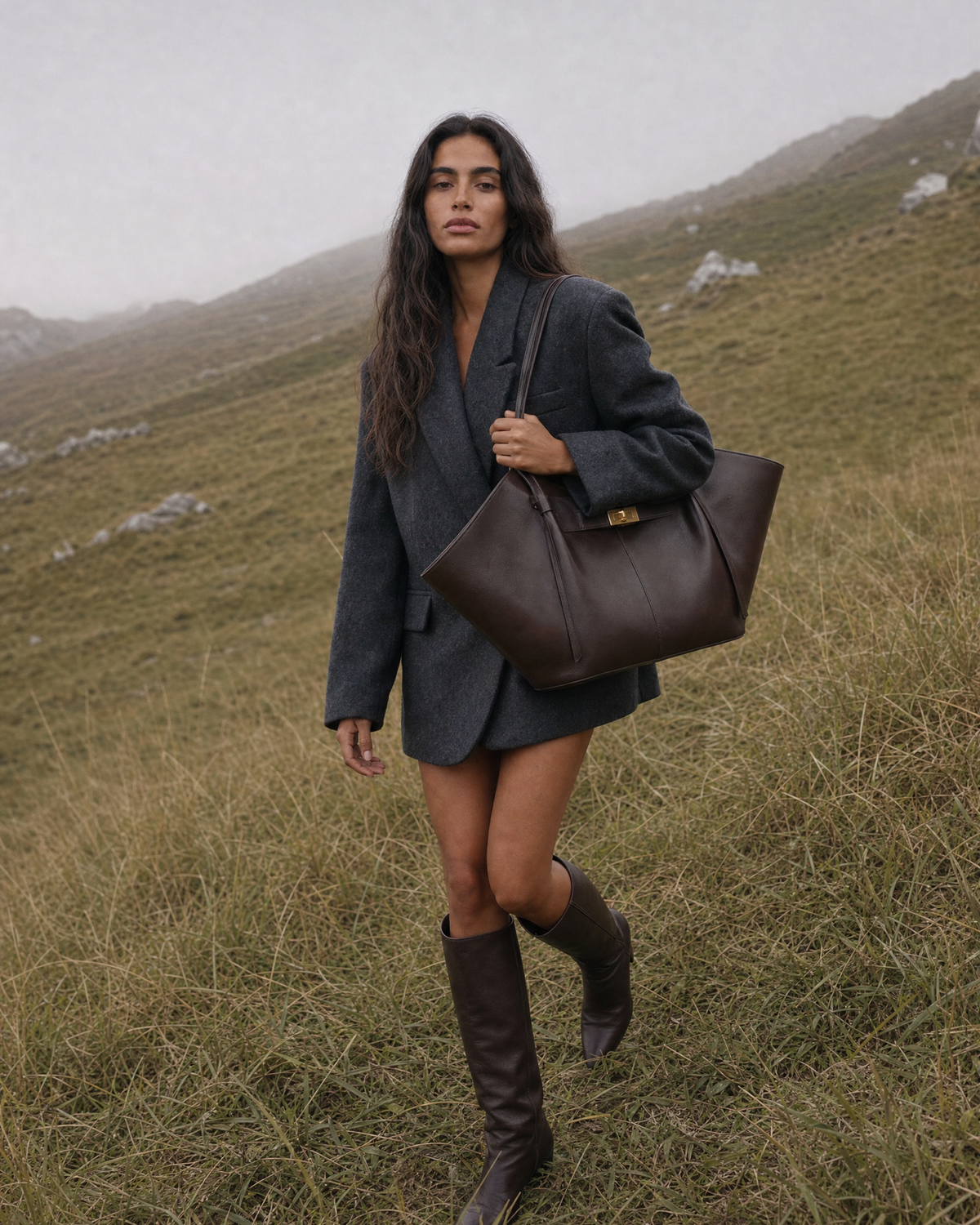 Woman walking uphill through tall grass with The Aurore Wing in Espresso on her shoulder