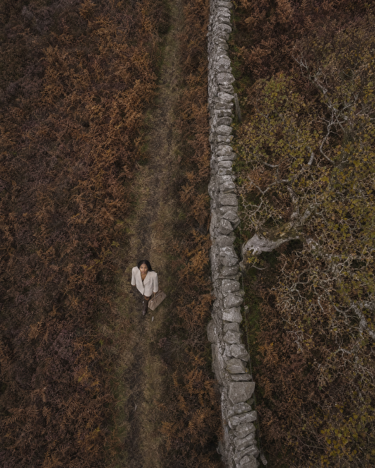 Aerial view of a woman walking along a dry-stone wall with The Brume East-West in Galet