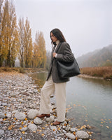 The Embellie in Noir, black woven leather tote worn on the shoulder by the river