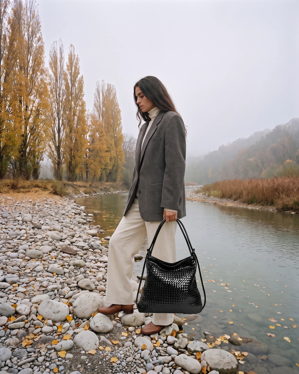 The Embellie Grand in Noir, large black woven leather tote carried by the double cord handle by the river