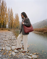The Embellie in Bordeaux, burgundy woven leather tote worn on the shoulder by the river