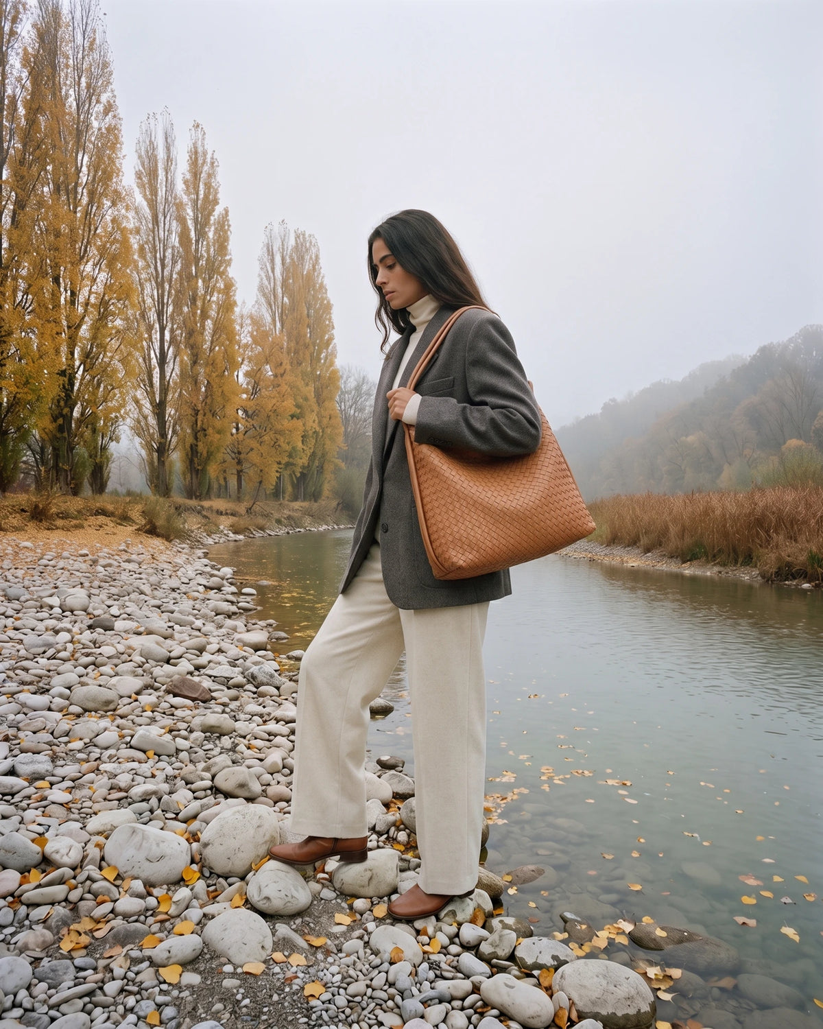 The Embellie in Cognac, tan brown woven leather tote worn on the shoulder by the river