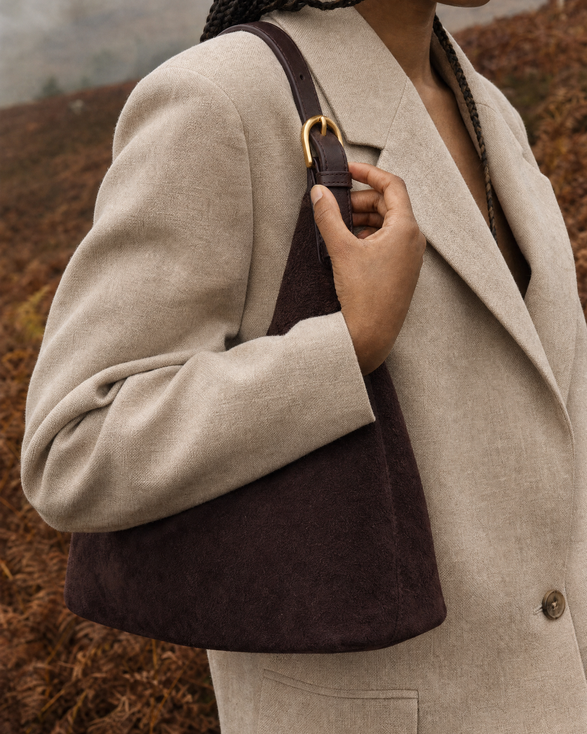 Hand on the gold buckle of The Brume Petite in Chocolate