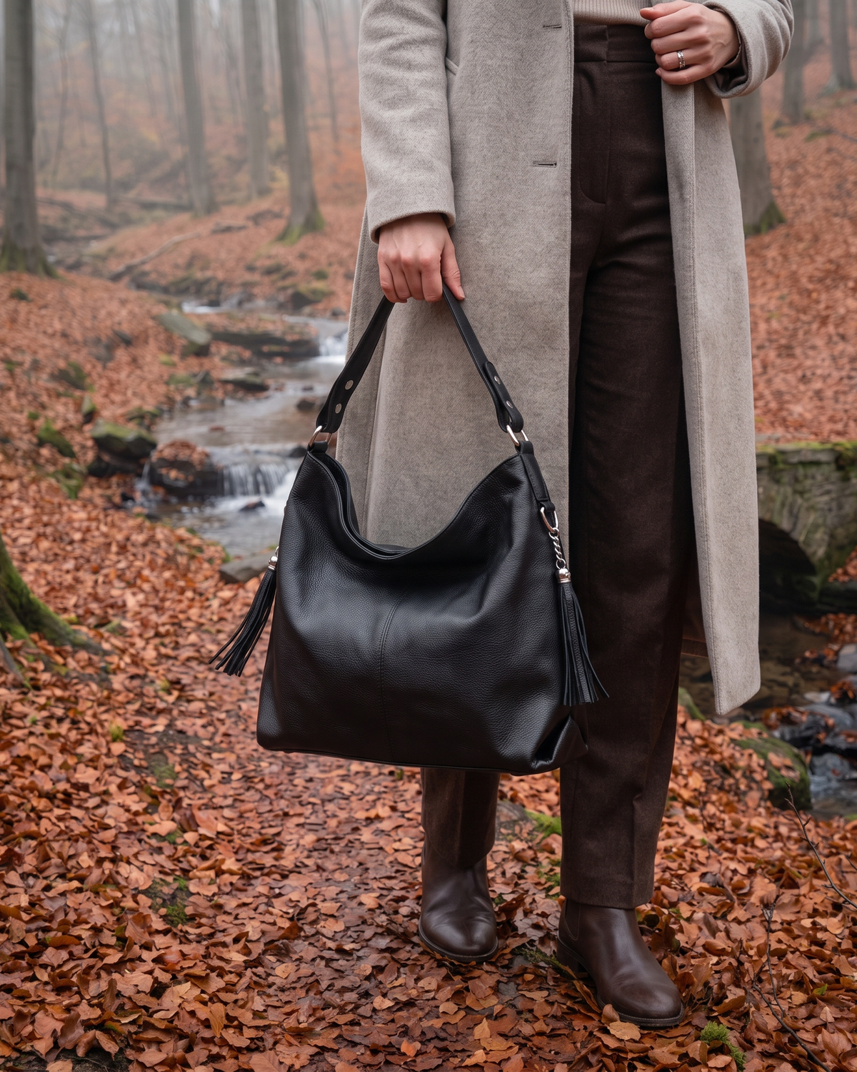 The Houle Soft in Noir, black leather hobo bag carried by the handle in a misty autumn beech forest