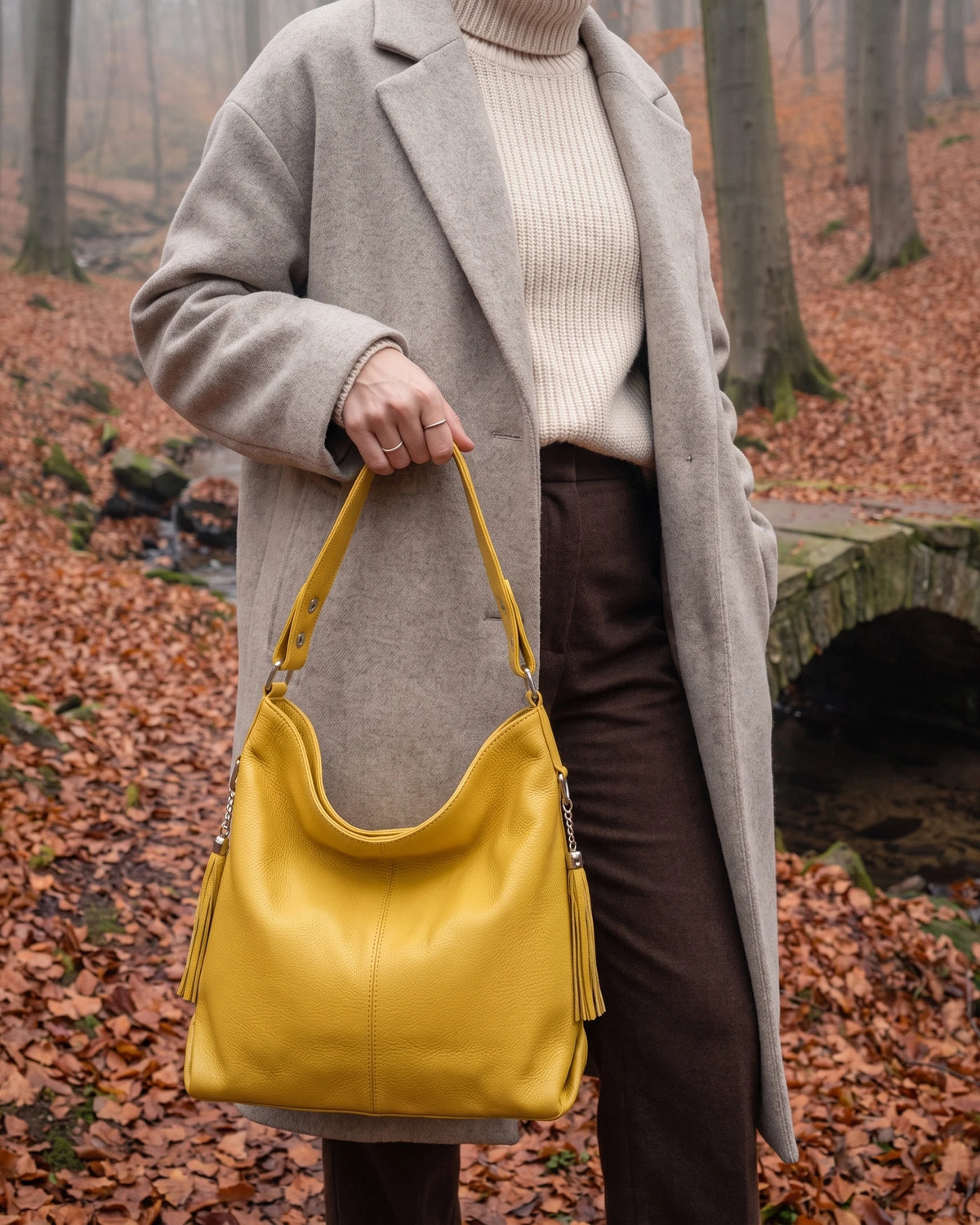 The Houle Soft in Citron, lemon yellow leather hobo bag carried by the handle in a misty autumn beech forest