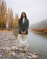 The Embellie in Écru, ivory woven leather tote held in front of her by the river