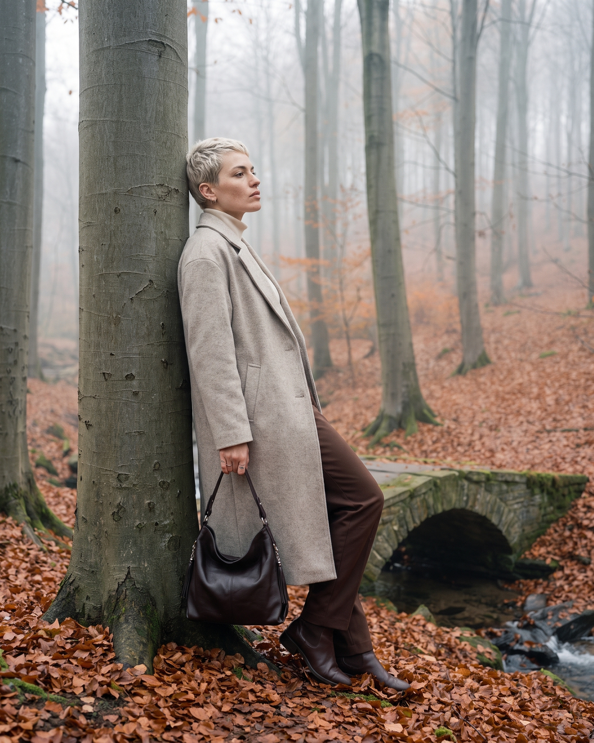 The Houle Soft in Espresso, espresso brown leather hobo bag in hand, model leaning against a beech tree in autumn mist