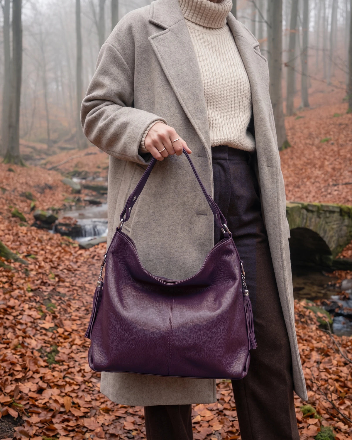 The Houle Soft in Prune, plum leather hobo bag carried by the short handle in a misty autumn beech forest
