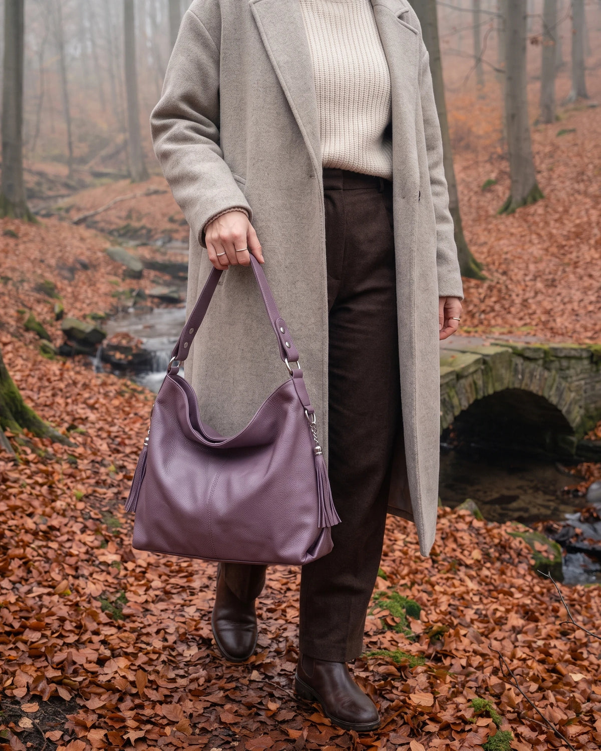The Houle Soft in Lilas, muted lilac leather hobo bag carried by the handle in a misty autumn beech forest