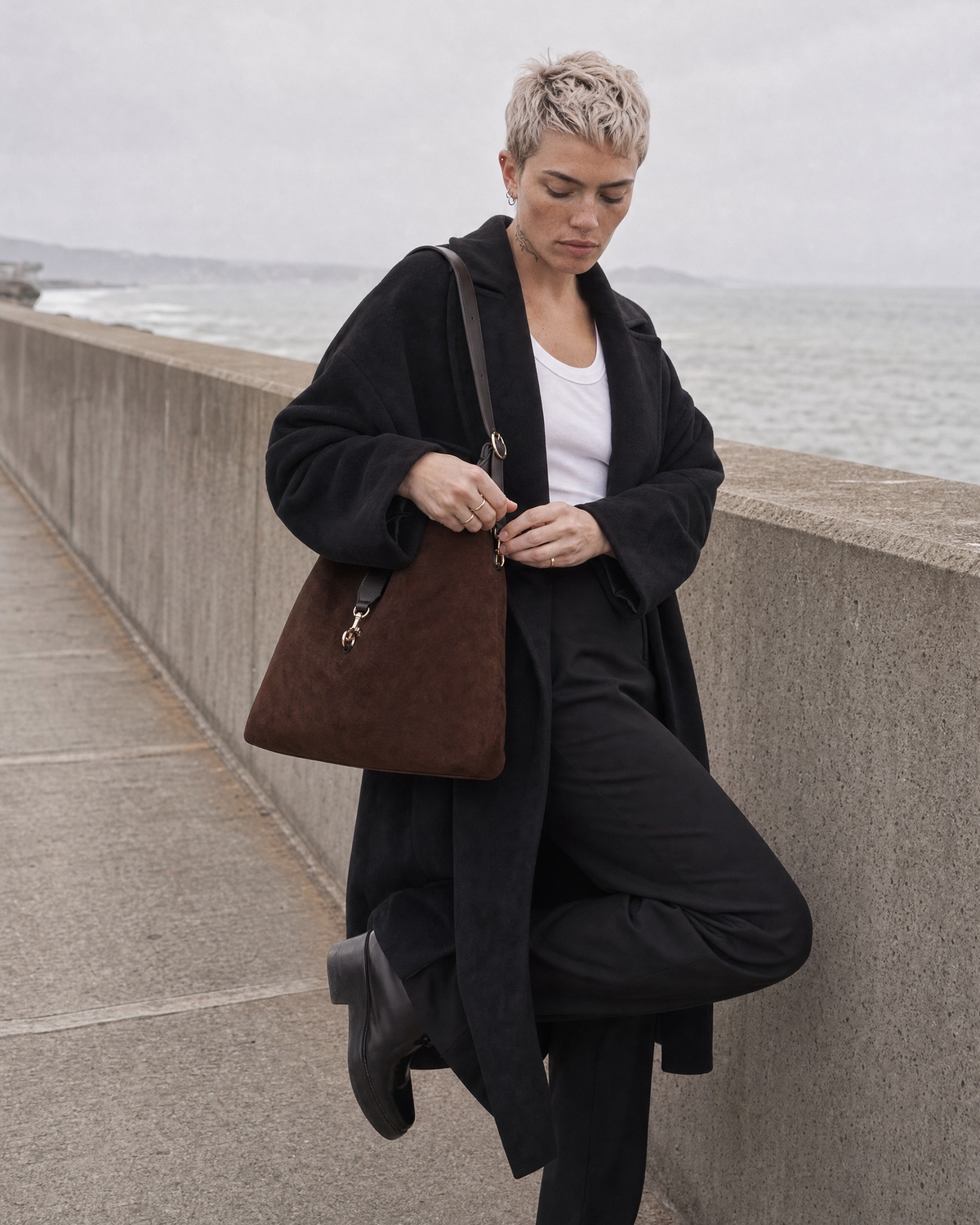 Woman fastening the hook clip of The Brume Clip Hobo in Chocolate by the sea