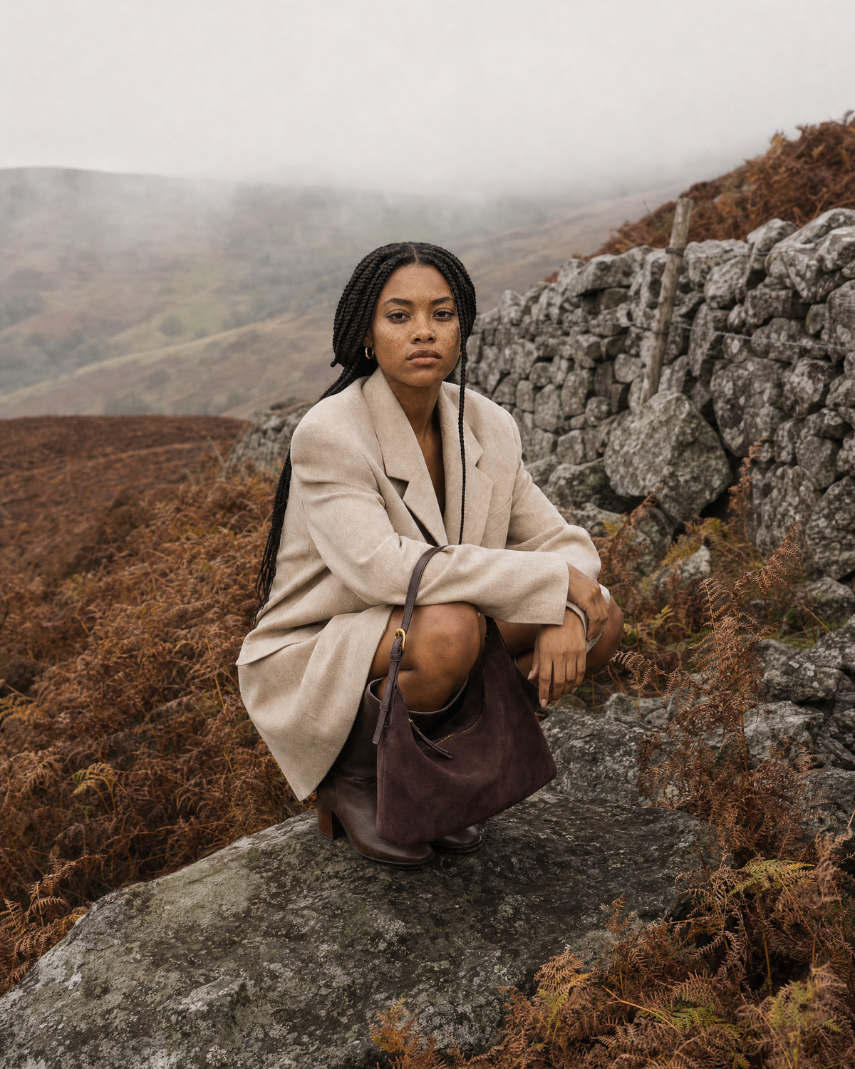 Woman crouching on a rock on a misty moor with The Brume Petite in Chocolate