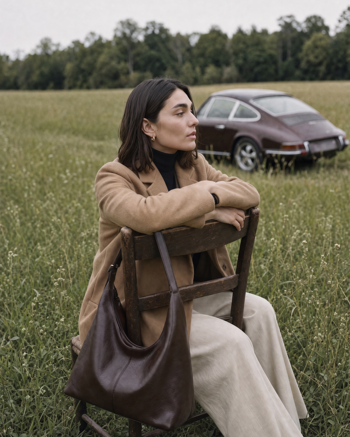 Woman sitting backwards on a wooden chair in a meadow, The Houle in Espresso hanging from the chair