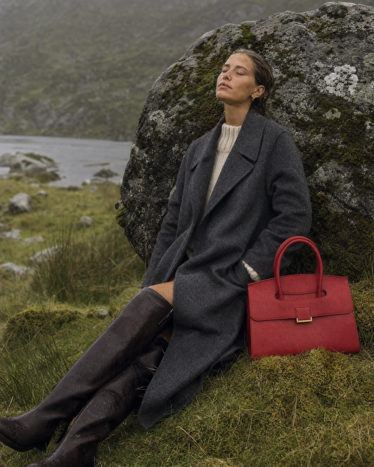 Woman resting against a boulder in the rain beside The Aurore Briefcase in Rouge