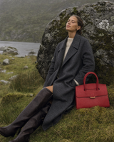 Woman resting against a boulder in the rain beside The Aurore Briefcase in Rouge
