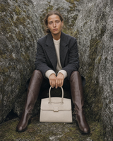 Woman sitting between two boulders with The Aurore Briefcase in Écru