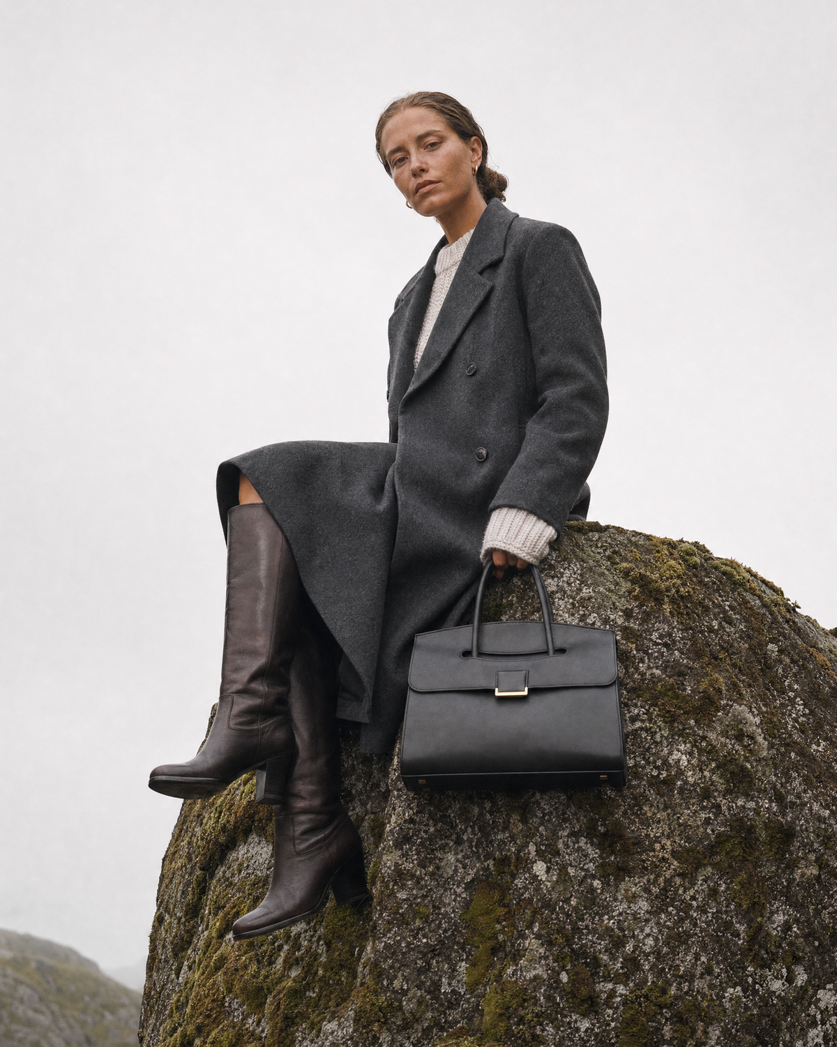 Woman sitting on a tall boulder with The Aurore Briefcase in Noir