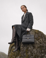 Woman sitting on a tall boulder with The Aurore Briefcase in Noir