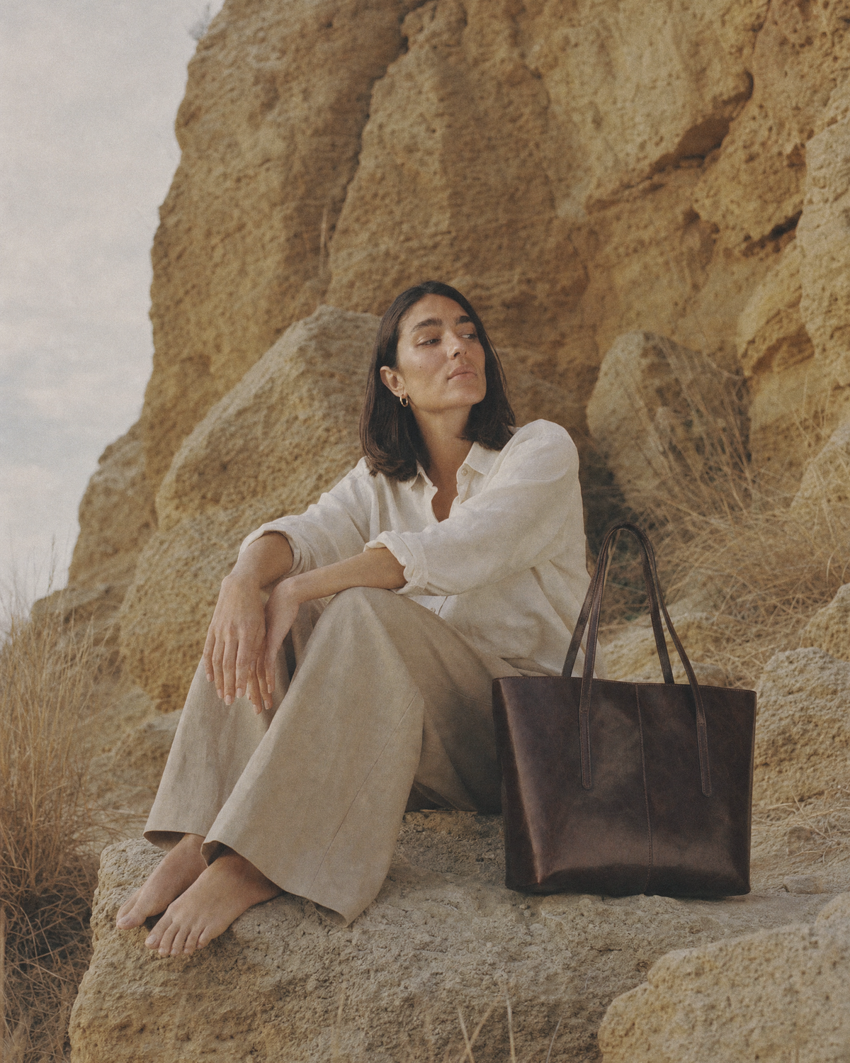 Woman sitting on a sandstone rock beside The Marée A4 tote