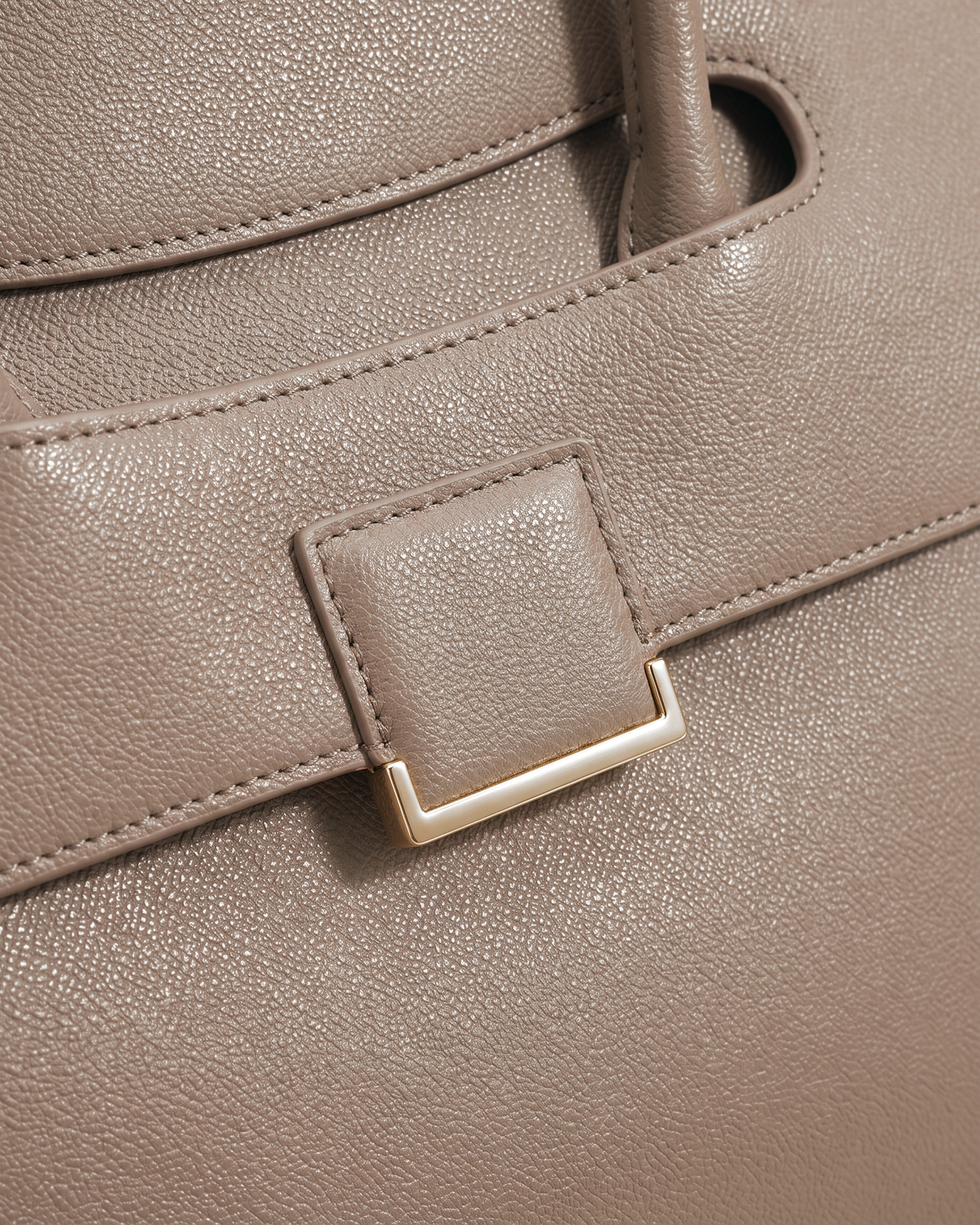 Close-up of the square gold plate on the flap of The Aurore Briefcase in Sable