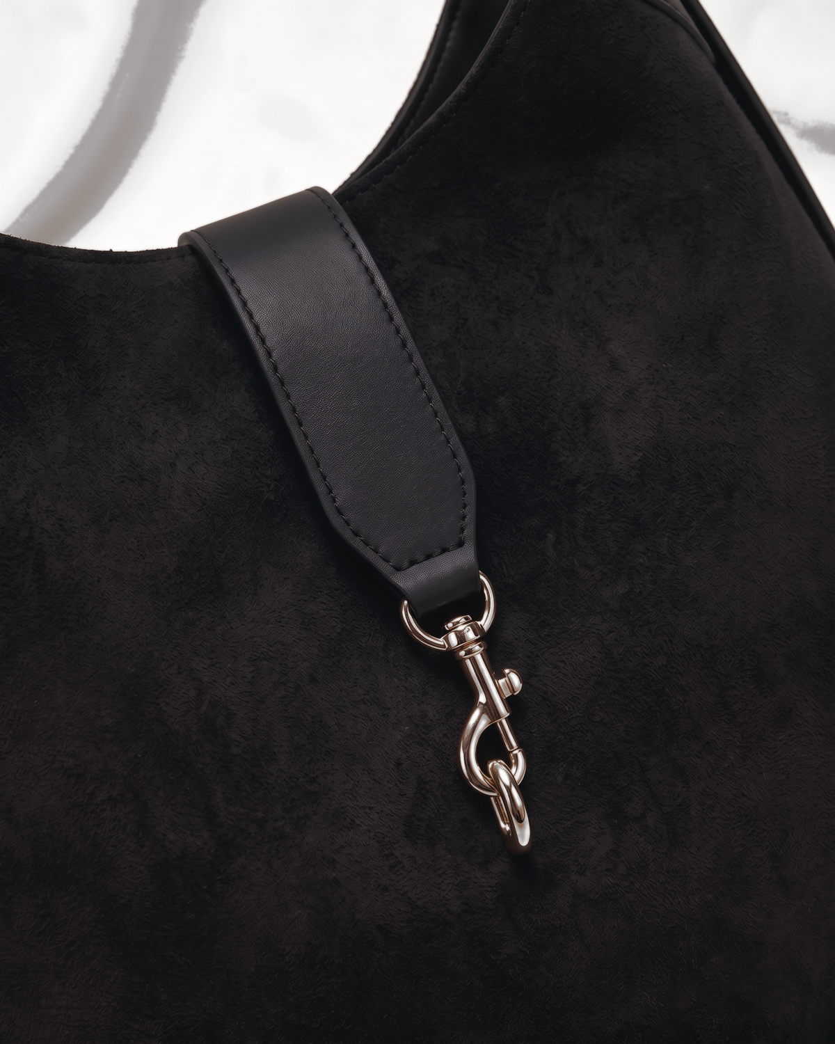 Close-up of the gold hook clip on the leather tab of The Brume Clip Hobo in Noir