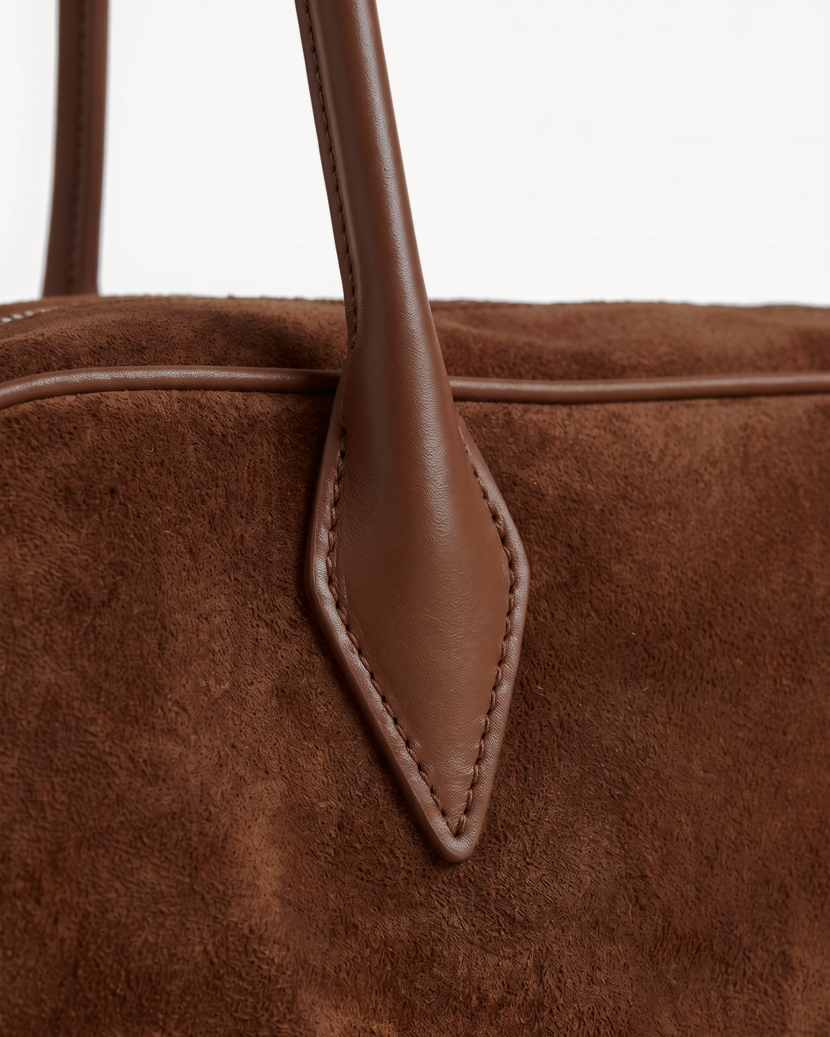 Close-up of the pointed leather tab and long handle of The Brume East-West in Chocolate