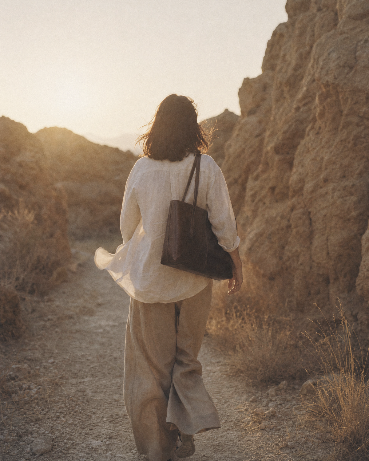 Woman walking away along a rocky path with The Marée A4 tote on her shoulder