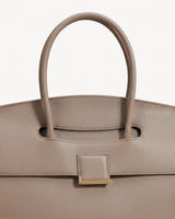 Close-up of the top handle passing through the flap of The Aurore Briefcase in Sable