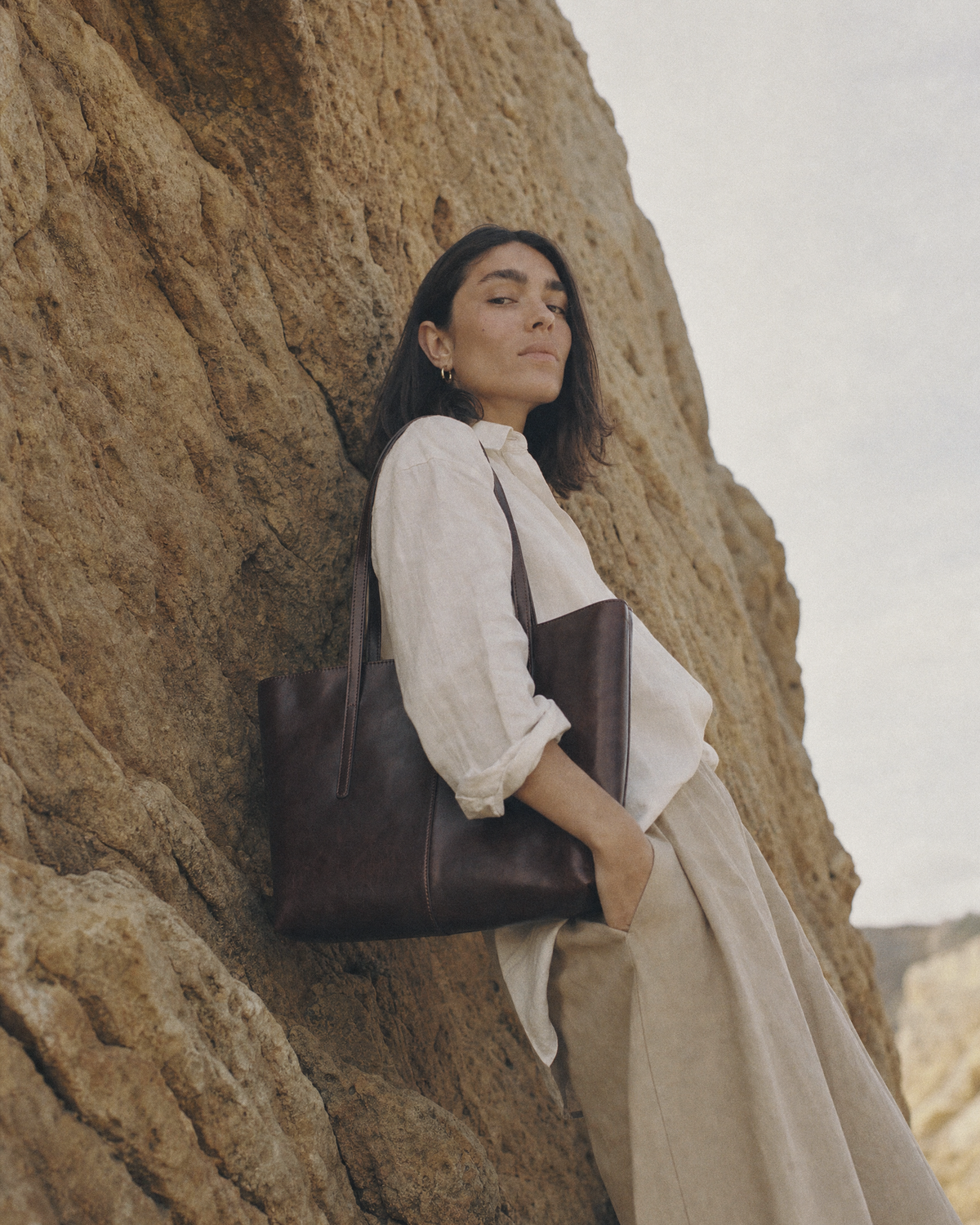 Woman leaning against a sandstone rock wall with The Marée A4 tote