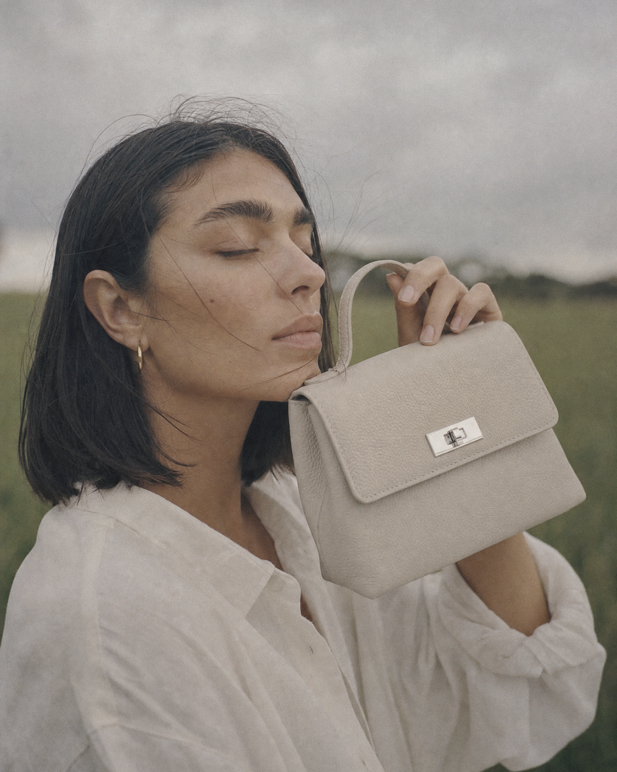 Woman holding The Brise in Écru beside her face, eyes closed