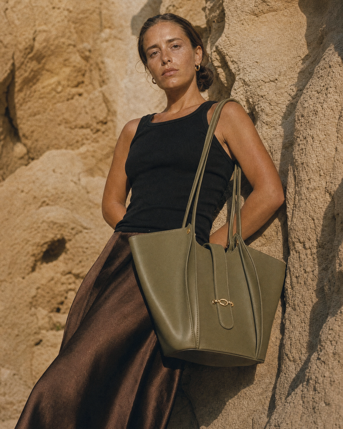 Woman leaning against a sandstone wall with The Havre Buckle in Olive