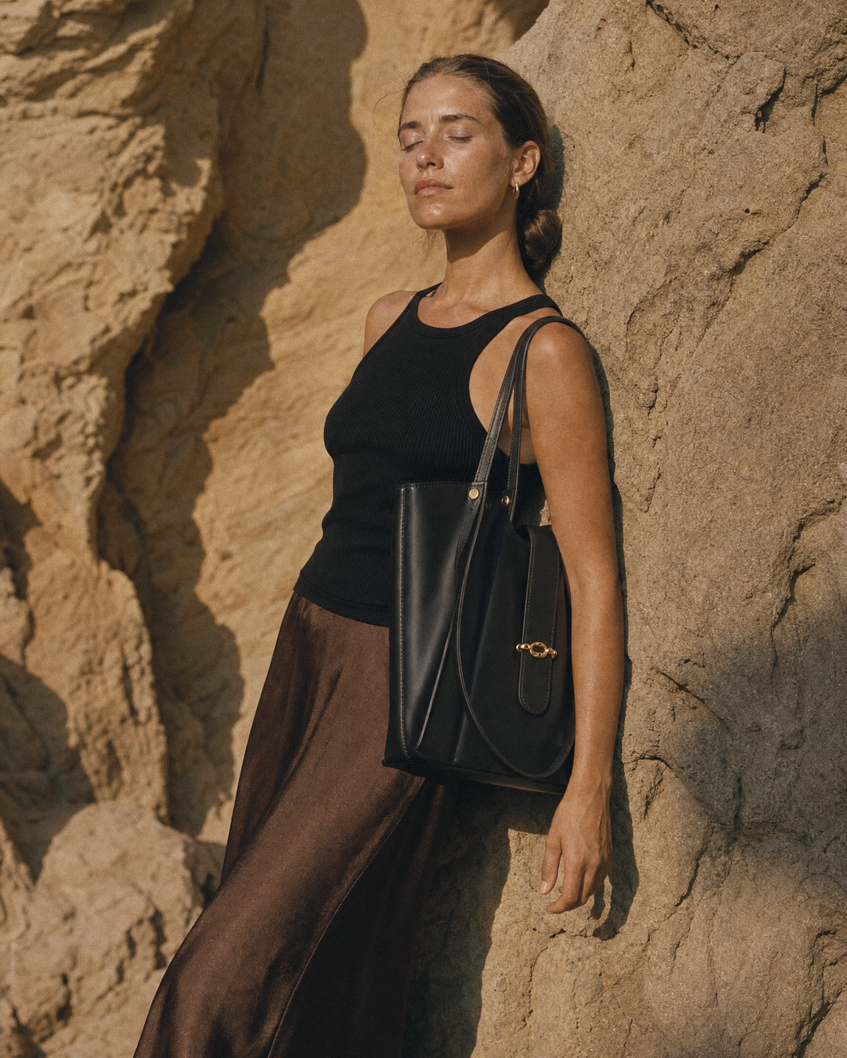Woman leaning against a sandstone wall with The Havre Buckle in Noir