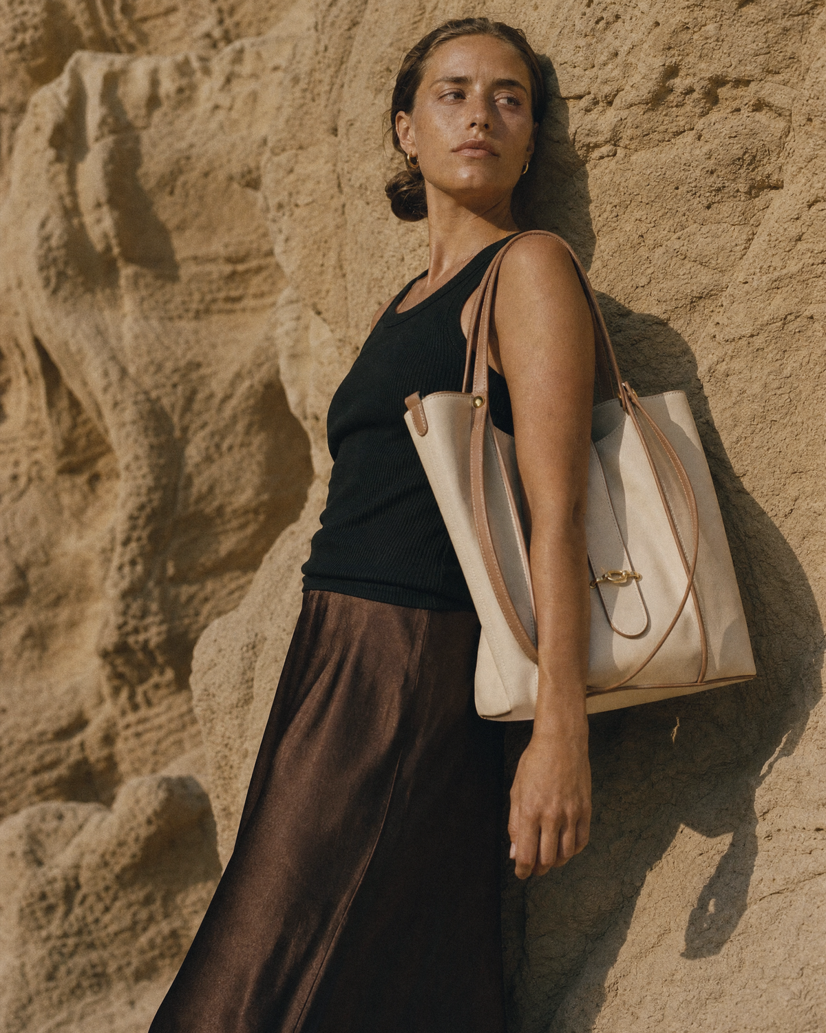Woman leaning against a sandstone wall with The Havre Buckle in Écru