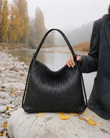 The Embellie in Noir Mat, matte black woven leather tote standing on a river boulder