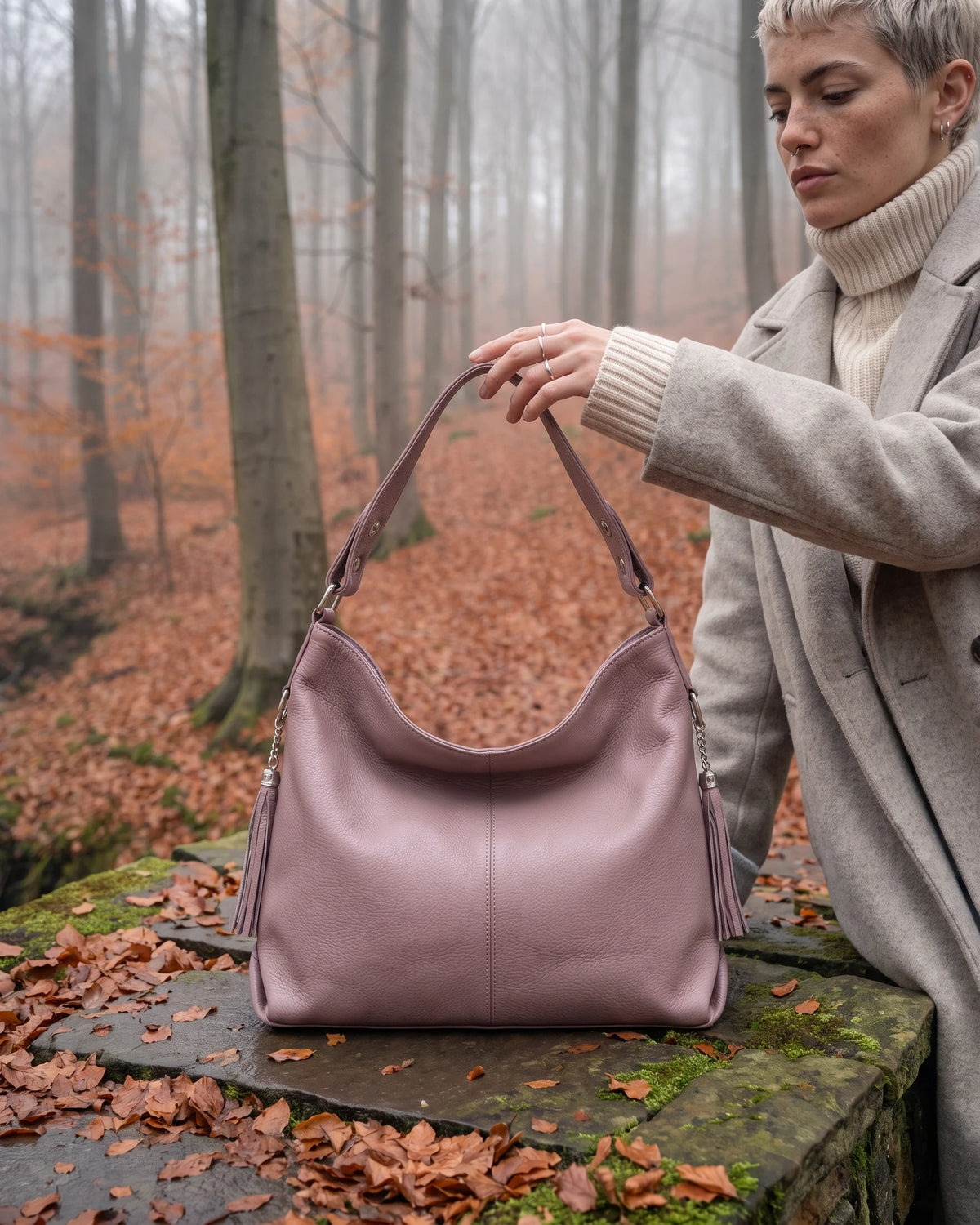 The Houle Soft in Rose, dusty rose leather hobo bag standing on the mossy stones of a forest footbridge