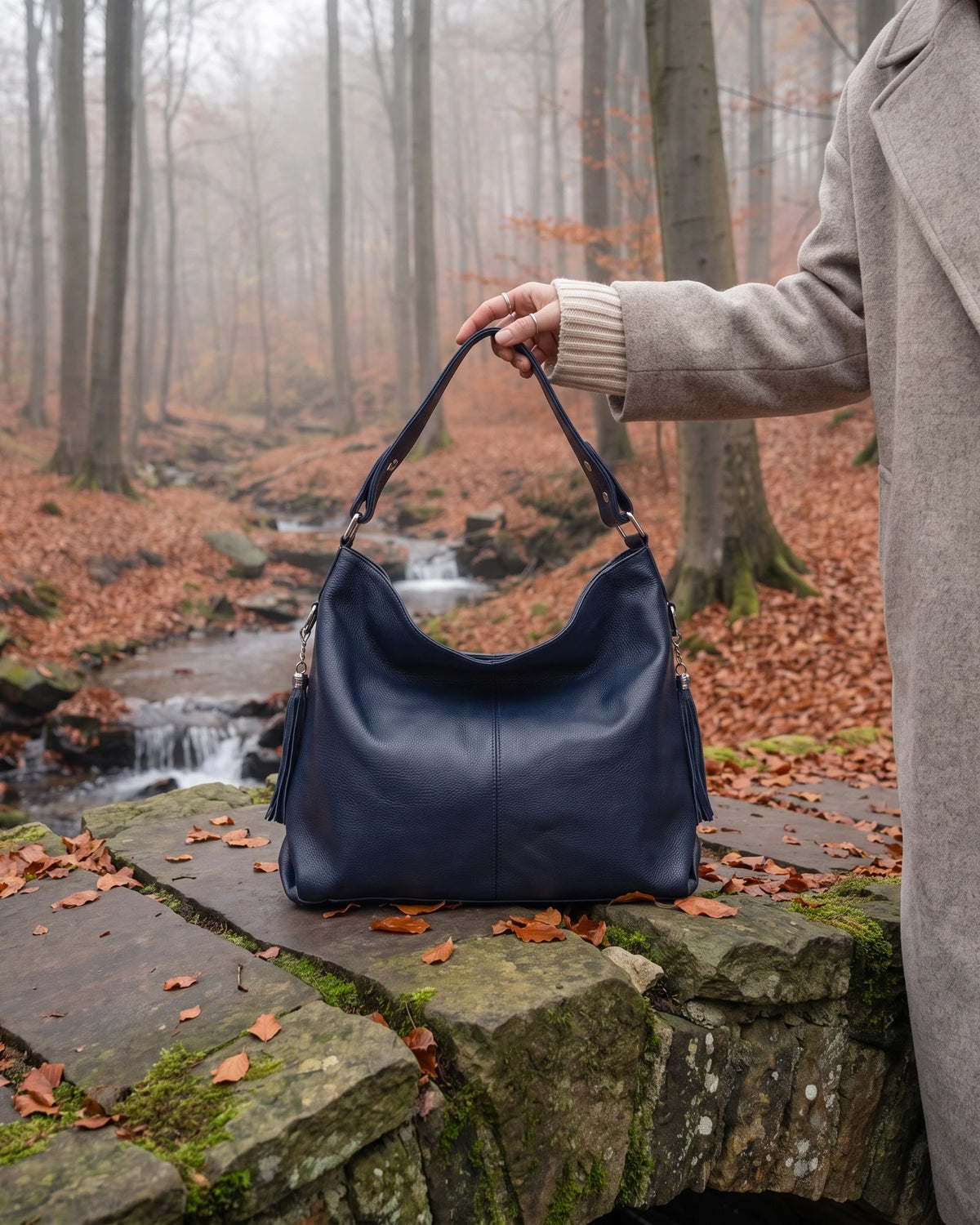 The Houle Soft in Nuit, midnight navy leather hobo bag held on the mossy stones of a forest footbridge