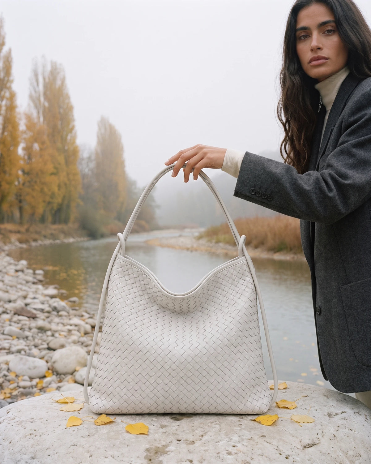 The Embellie in Écru, ivory woven leather tote standing on a river boulder