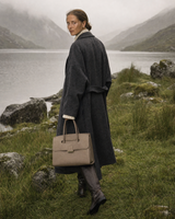 Woman walking along a loch shore carrying The Aurore Briefcase in Sable