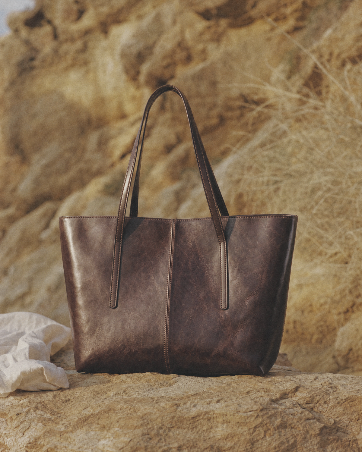 The Marée A4 espresso leather tote standing on a sandstone ledge in low sun