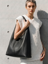 Woman in a white shearling vest holding The Anse in Noir against a concrete wall