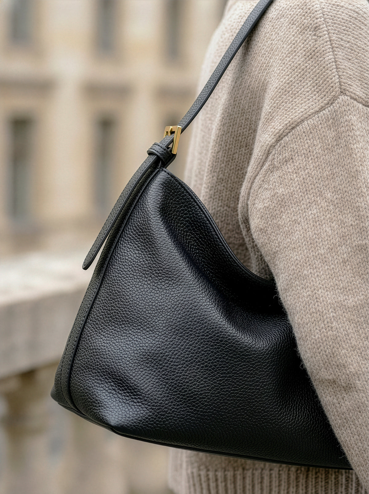 The Houle Petite in Noir worn on the shoulder over a beige sweater on a city street