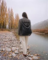 The Embellie Carryall in Noir, worn as a backpack by the river