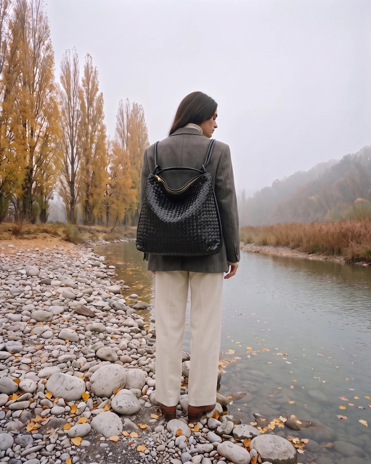 The Embellie Grand in Noir Mat, worn as a backpack by the river (shown in Noir)