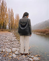 The Embellie Grand in Noir Mat, worn as a backpack by the river (shown in Noir)