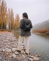 The Embellie Mini in Cognac, worn as a backpack by the river (shown in Noir)