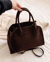 The Aurore Suede Satchel in Espresso, held by the handles